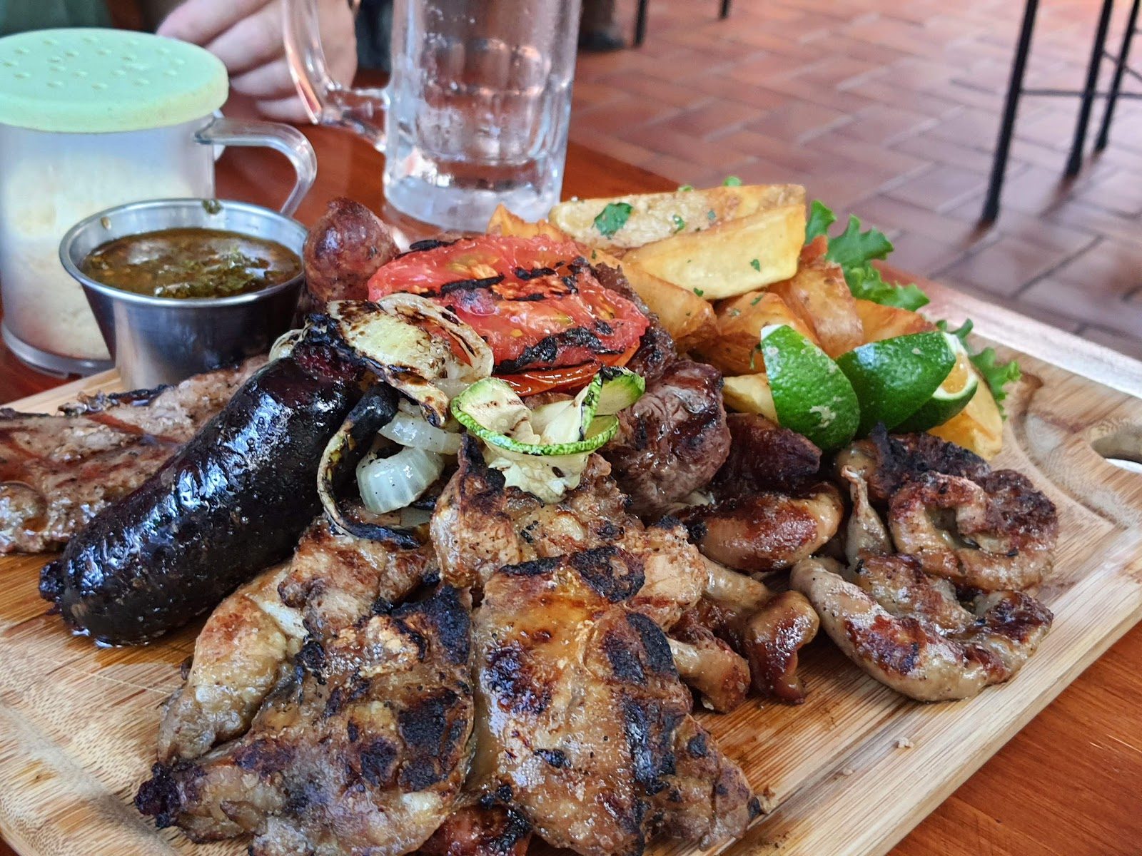 Parrillada servida en tabla con papas y una cerveza en la mesa
