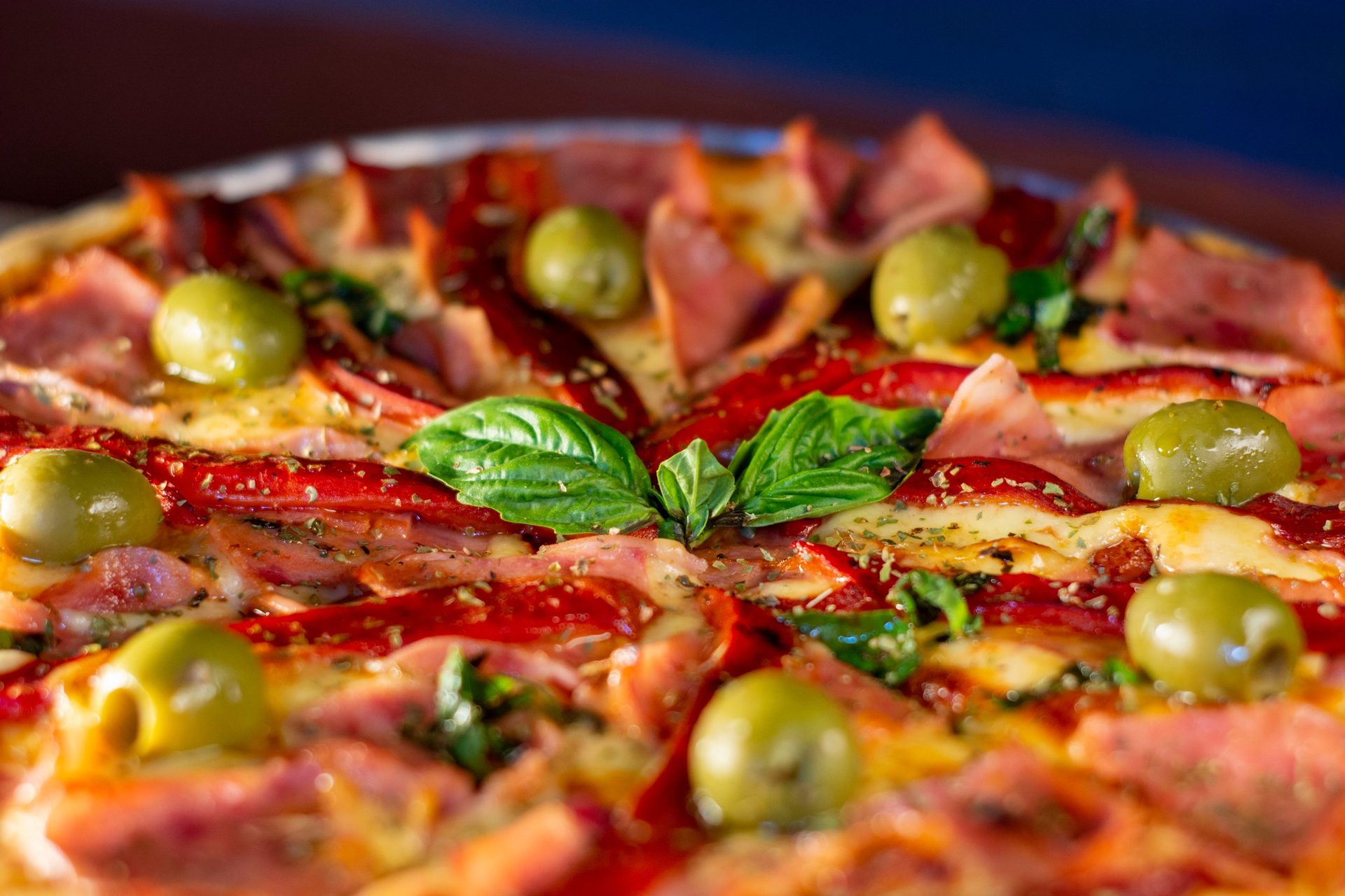 Detalle de pizza con aceitunas, albahaca y chile morrón asado